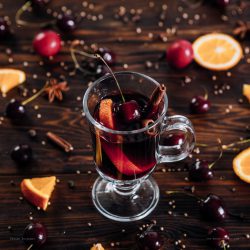 Mulled wine with a dynamic splash, spices and fruits on wooden background