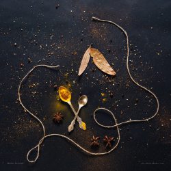 Assorted spices in spoons on dark black background. Seasonings for food. Curry, paprika, pepper, cardamom, anise, cloves, bay leaf, turmeric. Top view. Close-up.